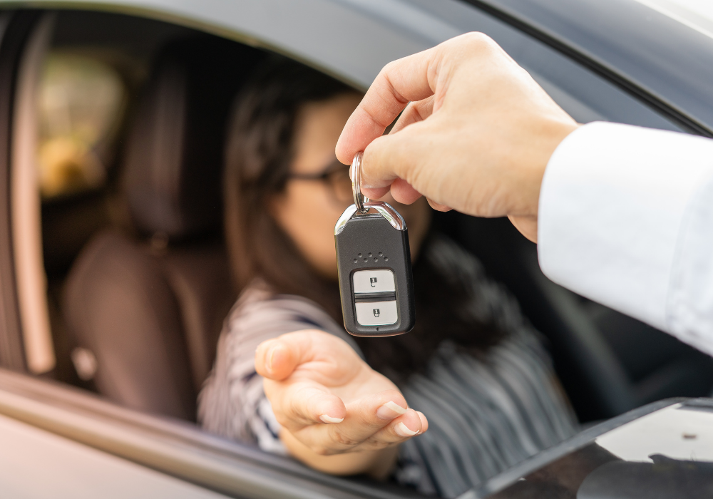 Auto locksmith replacing car key for lady customer and handing her new car key while she sits in her car